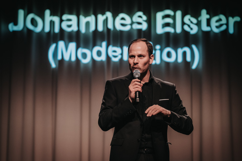 Johannes Elster, Moderator, hält Rede mit Mikrofon auf der Bühne. Event, Show.