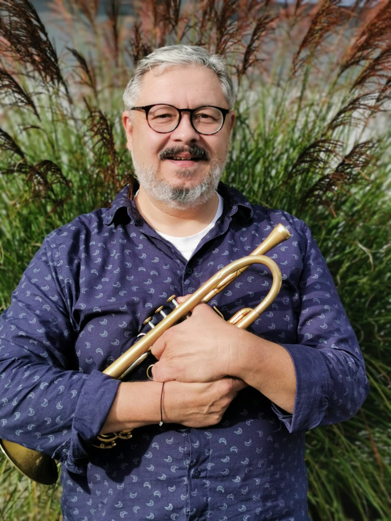 Mann mit Trompete. Musiker mit Brille, grauen Haaren und Bart. Musikinstrument im Freien.