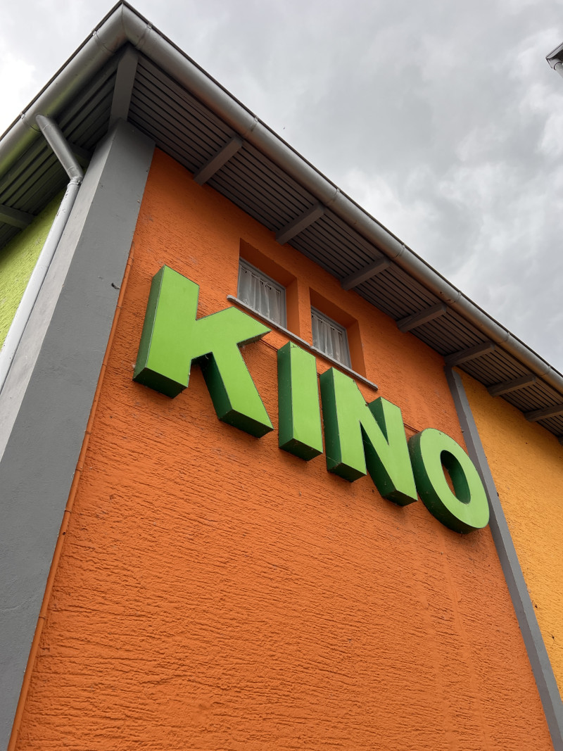 Grünes Kino Schild an orangefarbener Fassade. Architektur eines Kinos bei bewölktem Himmel.