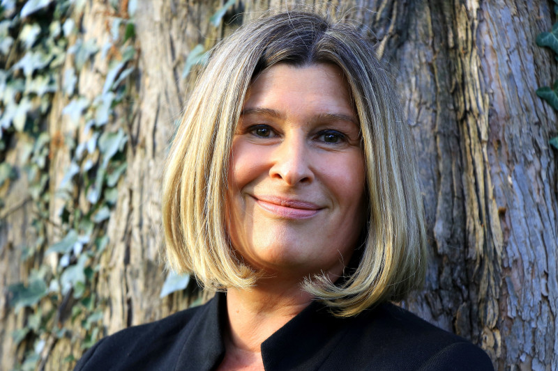 Frau lächelt, blondes Haar, vor Baum. Portrait einer sympathischen, reifen Frau im Freien.