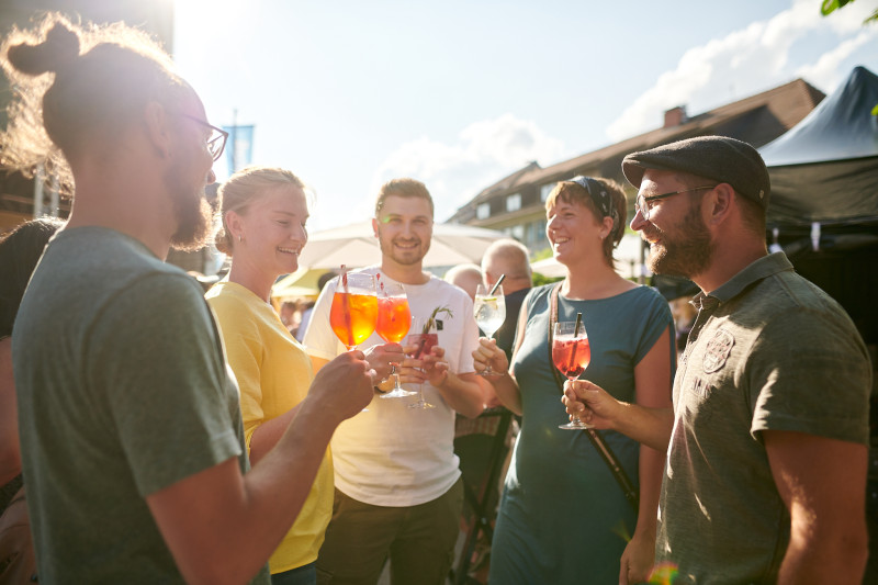 Freunde stoßen mit Aperol Spritz an. Sommerliche Getränke, Feier im Freien, gute Laune.
