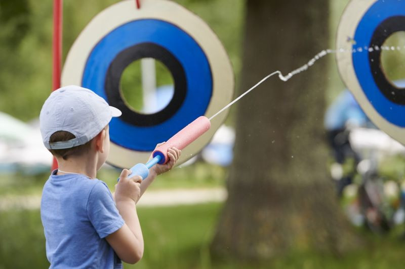 Junge zielt mit Wasserpistole auf Zielscheibe. Sommerspaß, Wasserspiel im Freien.