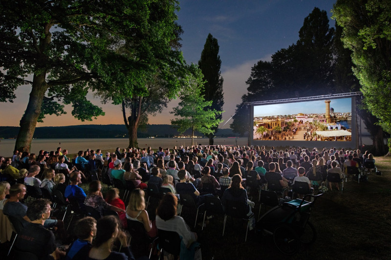 Open-Air Kino: Publikum genießt Filmvorführung unter Sternen am See. Sommerkino-Erlebnis.